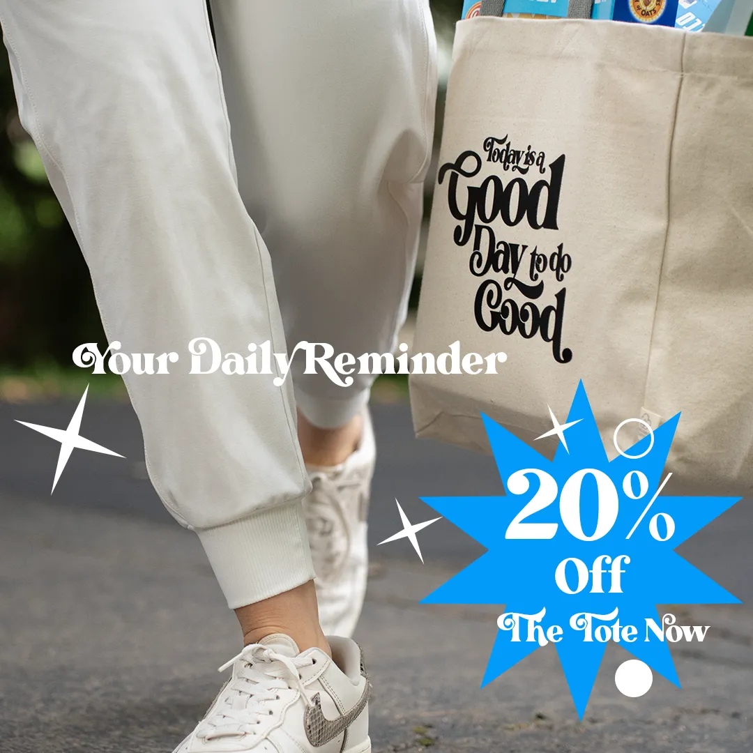 Person walking outdoors with white sneakers and light pants, carrying a beige tote bag that reads 'Today is a Good Day to do Good.'