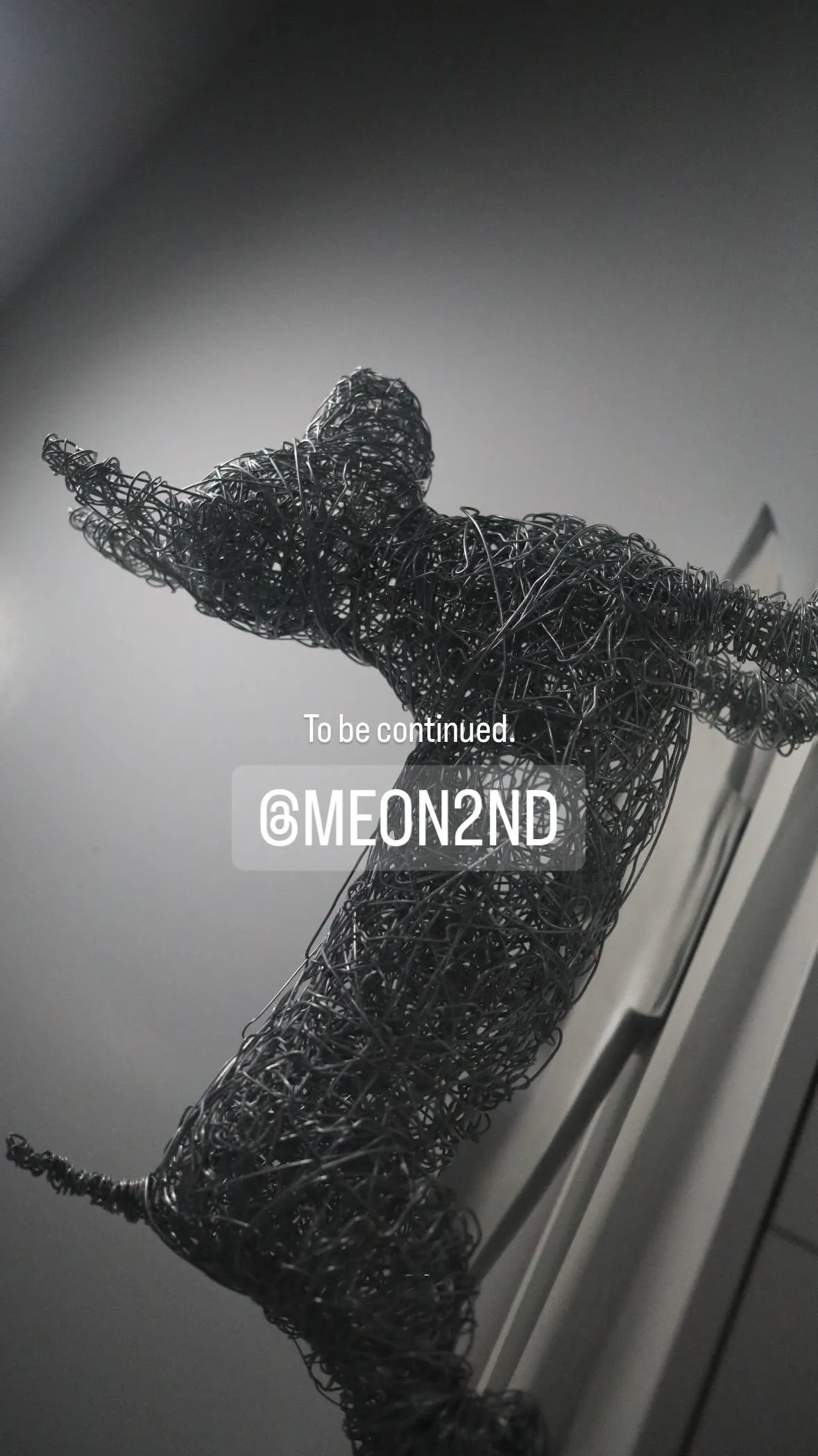 Wire sculpture of a dancing human figure with arms outstretched against a plain background.