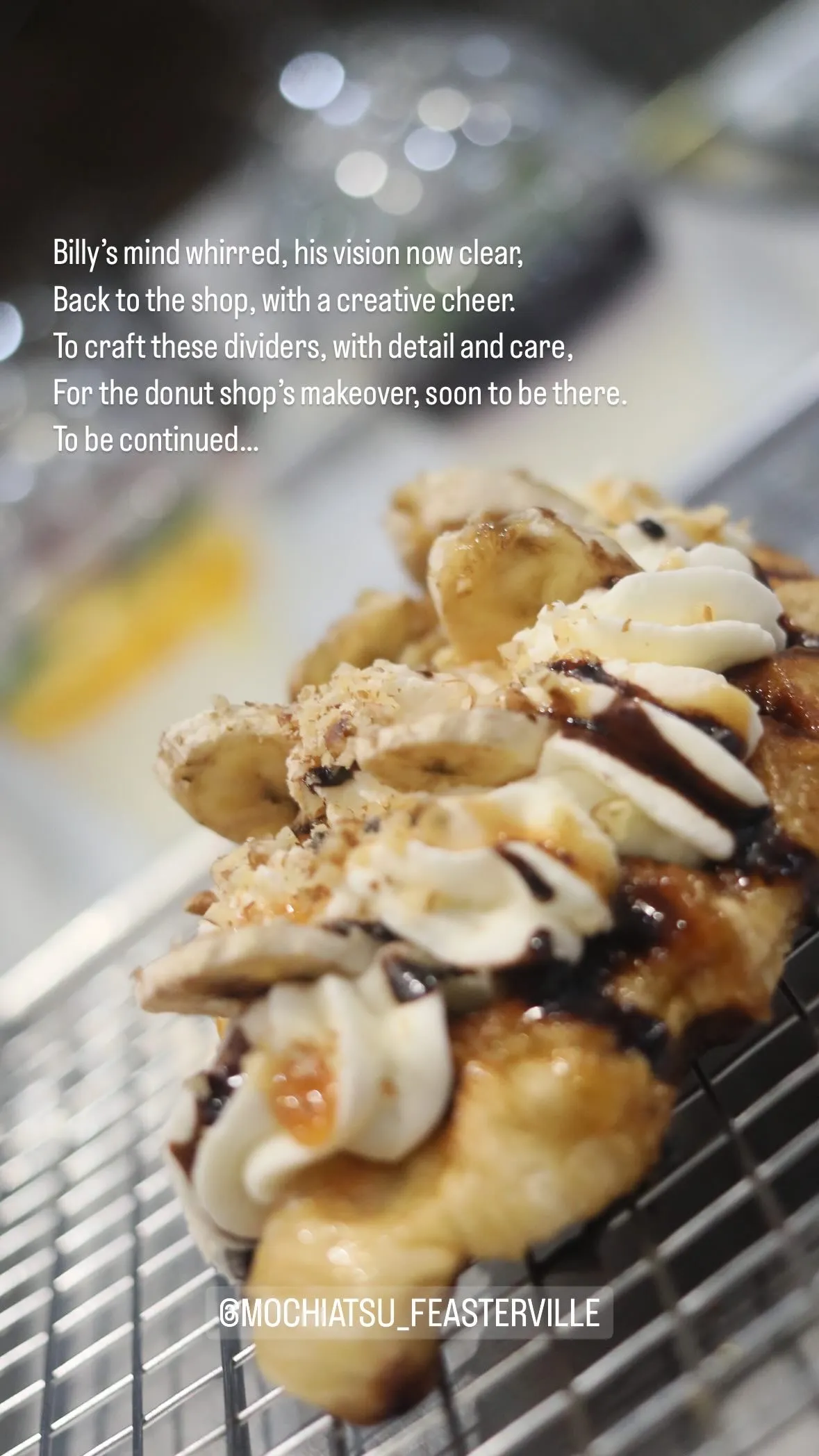 Close-up of a donut topped with banana slices, whipped cream, chocolate drizzle, and nuts on a cooling rack.