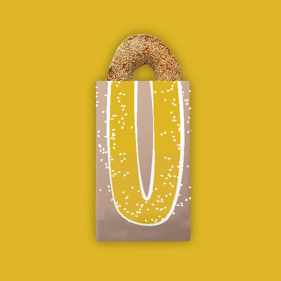 Sesame bagel partially inside a paper bag with a yellow and beige sesame seed design on a mustard yellow background.