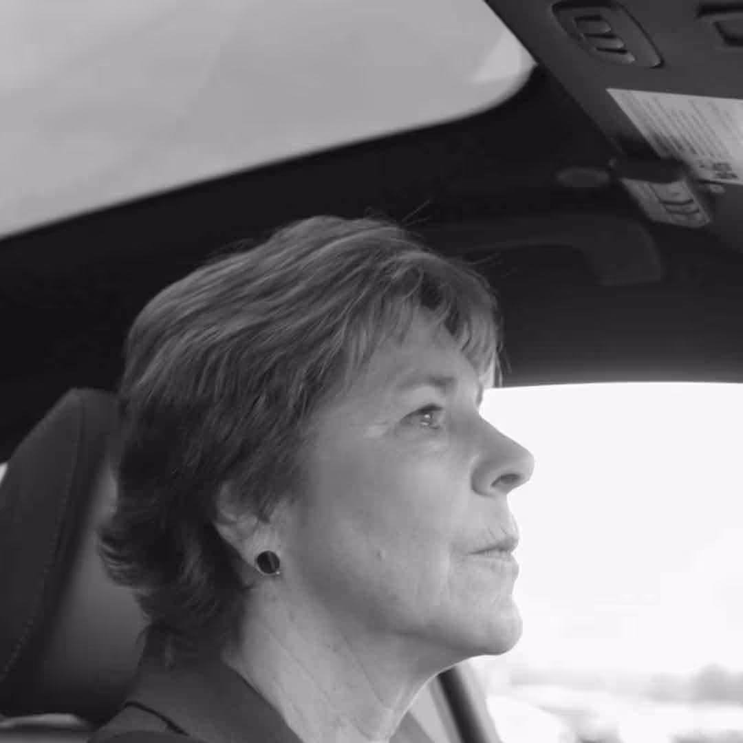 Profile of a middle-aged woman with short hair driving a car and looking ahead.